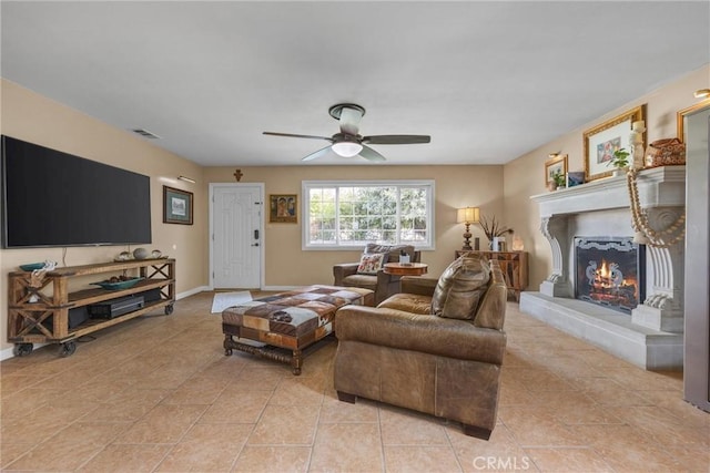 living room featuring a warm lit fireplace, baseboards, visible vents, ceiling fan, and light tile patterned flooring