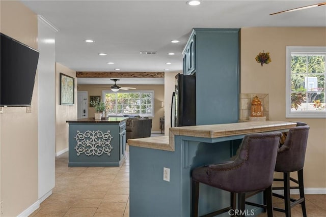 kitchen with a peninsula, visible vents, tile counters, freestanding refrigerator, and a kitchen bar