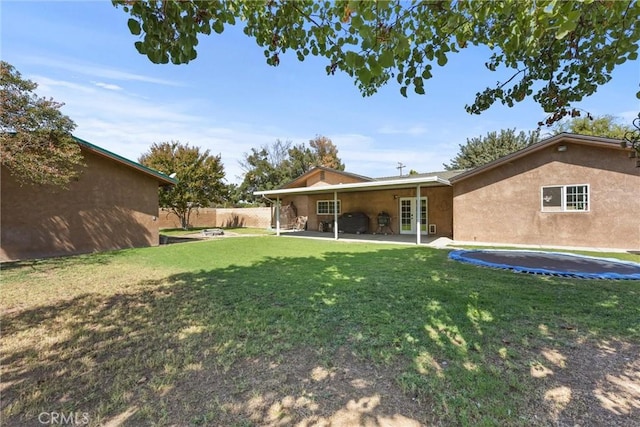 rear view of house with a trampoline, a yard, fence, and stucco siding