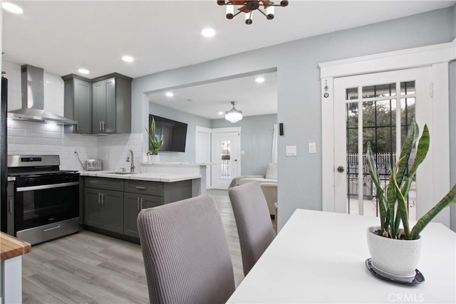 kitchen with gray cabinetry, stainless steel range with gas cooktop, decorative backsplash, wall chimney exhaust hood, and a sink