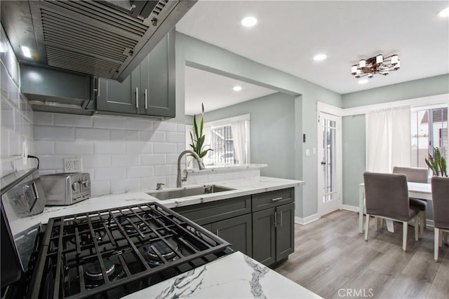 kitchen with light stone countertops, light wood-style flooring, a sink, exhaust hood, and tasteful backsplash