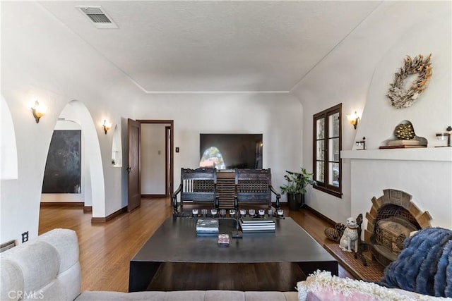 living area with arched walkways, a fireplace, wood finished floors, visible vents, and baseboards