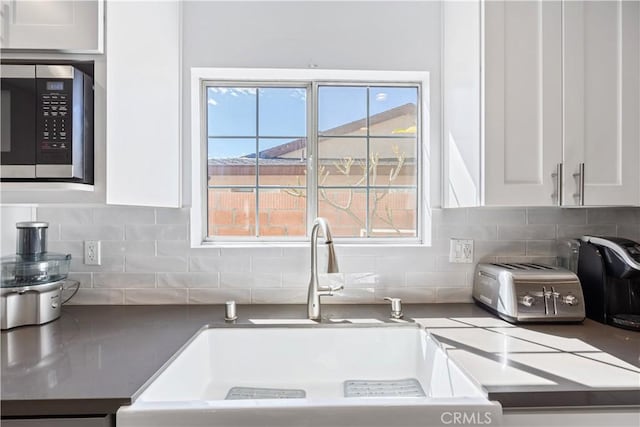 kitchen with a toaster, white cabinets, decorative backsplash, stainless steel microwave, and a sink