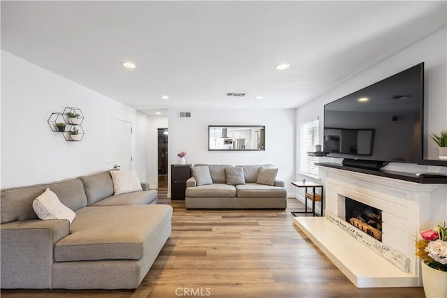 living room featuring light wood-style floors, visible vents, a fireplace with raised hearth, and recessed lighting