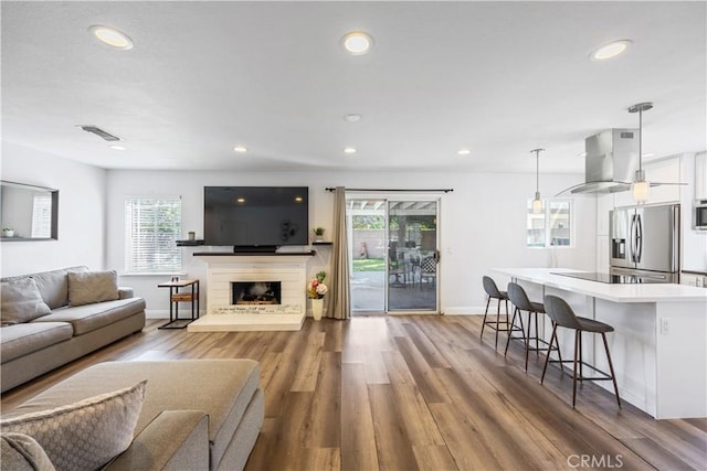 living area featuring visible vents, a fireplace with raised hearth, wood finished floors, and recessed lighting