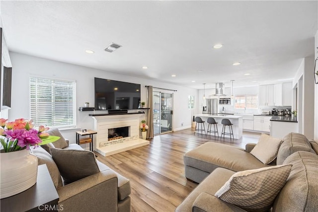 living area featuring a fireplace with raised hearth, light wood-style flooring, recessed lighting, visible vents, and baseboards