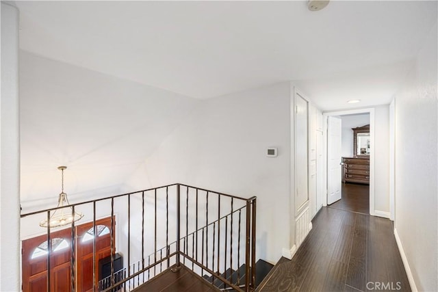 corridor featuring an upstairs landing, a notable chandelier, baseboards, and wood finished floors