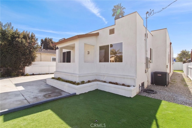 view of front of house featuring a patio, stucco siding, central air condition unit, a front yard, and fence