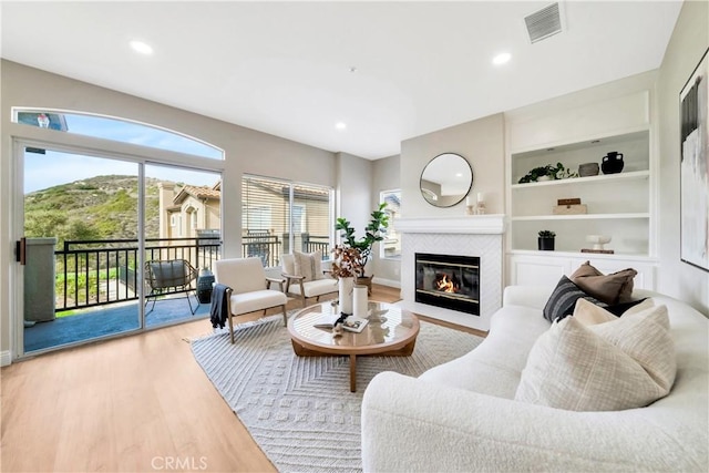 living room with built in features, light wood finished floors, recessed lighting, visible vents, and a glass covered fireplace