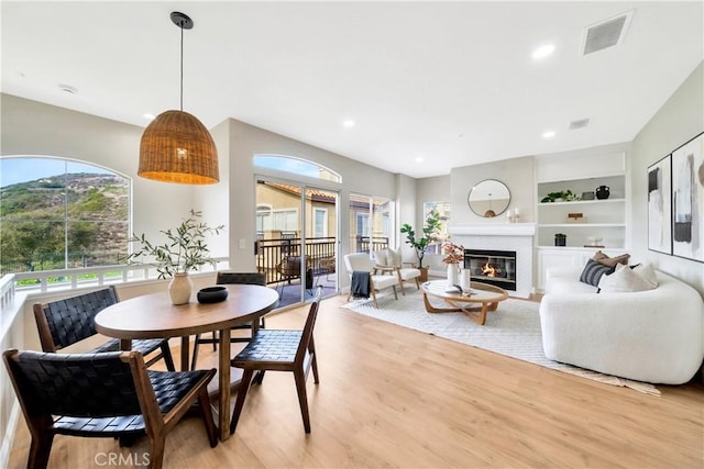 dining room featuring built in shelves, recessed lighting, visible vents, light wood-type flooring, and a glass covered fireplace