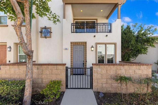 view of front of house with a fenced front yard, a gate, a balcony, and stucco siding