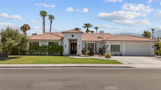 mediterranean / spanish-style house featuring stucco siding, an attached garage, driveway, a tiled roof, and a front lawn