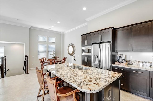 kitchen with crown molding, appliances with stainless steel finishes, a kitchen island with sink, a sink, and light stone countertops