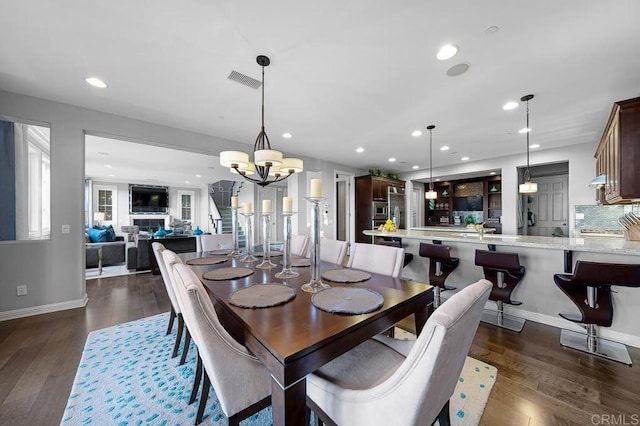 dining room with dark wood-style floors, a glass covered fireplace, visible vents, and recessed lighting