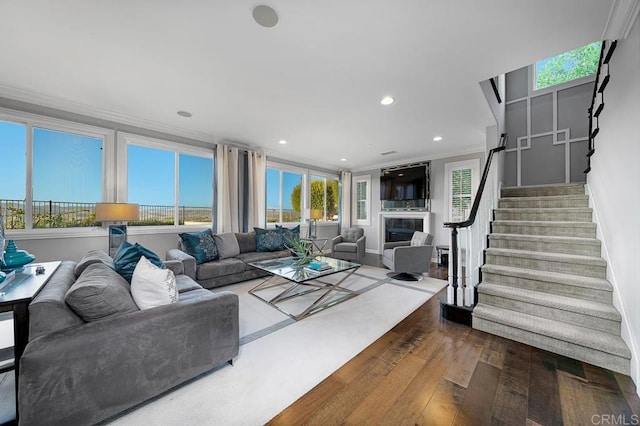 living room with a fireplace, ornamental molding, a healthy amount of sunlight, wood finished floors, and stairs