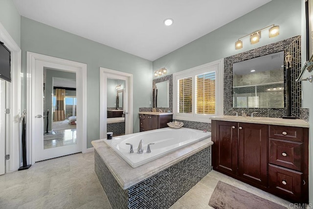 full bath featuring a bath, two vanities, and a wealth of natural light