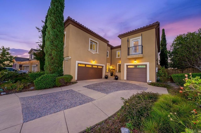 mediterranean / spanish house featuring an attached garage, a balcony, fence, a tile roof, and stucco siding