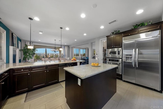 kitchen with built in appliances, dark brown cabinetry, a kitchen island, visible vents, and pendant lighting