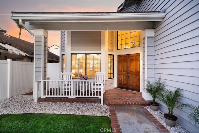 view of exterior entry featuring covered porch and fence