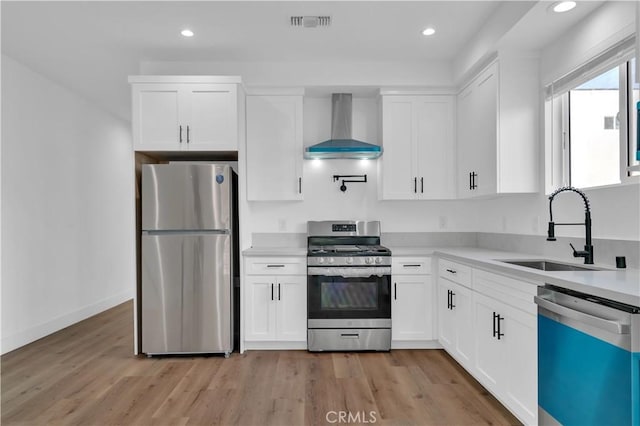 kitchen featuring a sink, white cabinetry, light countertops, appliances with stainless steel finishes, and wall chimney range hood