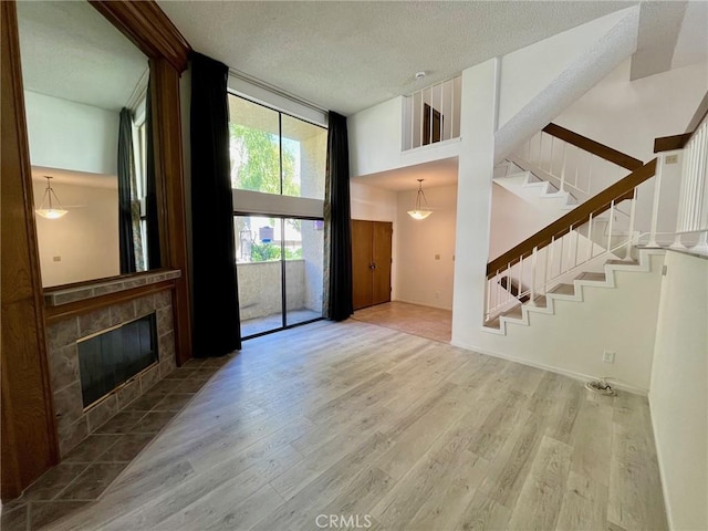 unfurnished living room with a textured ceiling, a fireplace, wood finished floors, a towering ceiling, and stairway