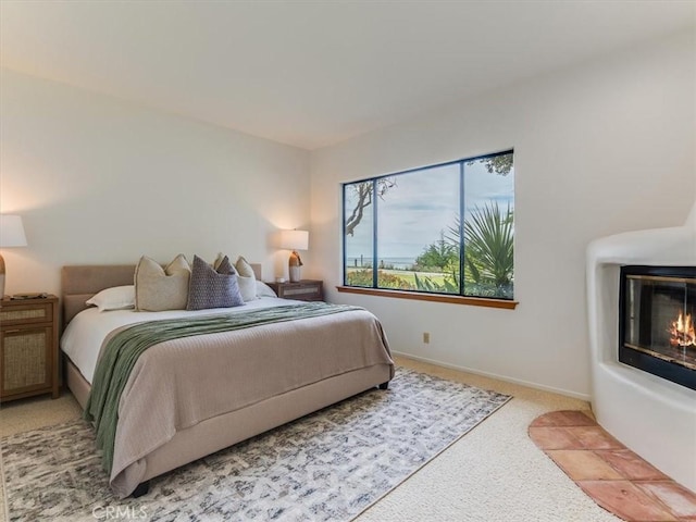 carpeted bedroom featuring a glass covered fireplace and baseboards