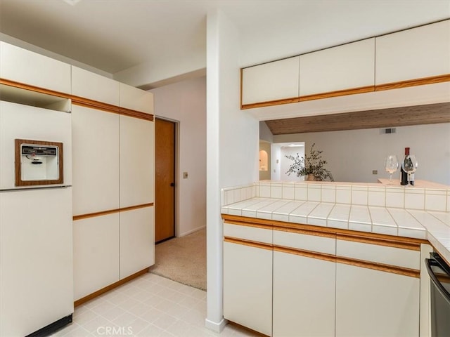 kitchen with white refrigerator with ice dispenser, tile counters, white cabinets, dishwasher, and a peninsula