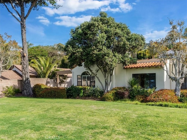 mediterranean / spanish house featuring a tiled roof, a front lawn, and stucco siding