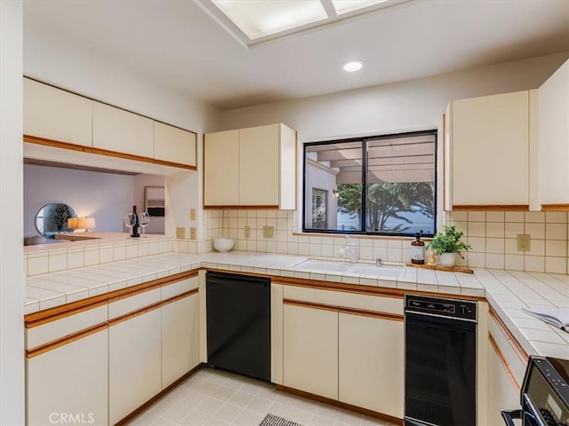 kitchen with cream cabinets, a sink, tile countertops, and decorative backsplash