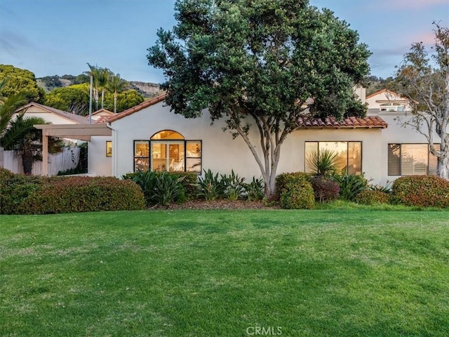 back of property at dusk featuring a lawn and stucco siding