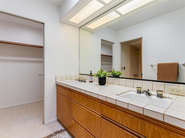 full bath featuring double vanity, baseboards, a walk in closet, and a sink