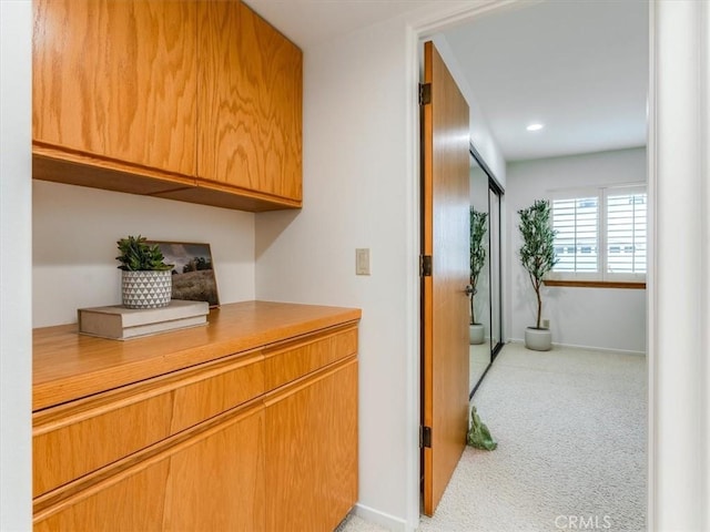 hallway featuring light colored carpet and baseboards