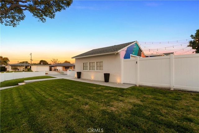 back of house at dusk featuring stucco siding, a yard, and fence