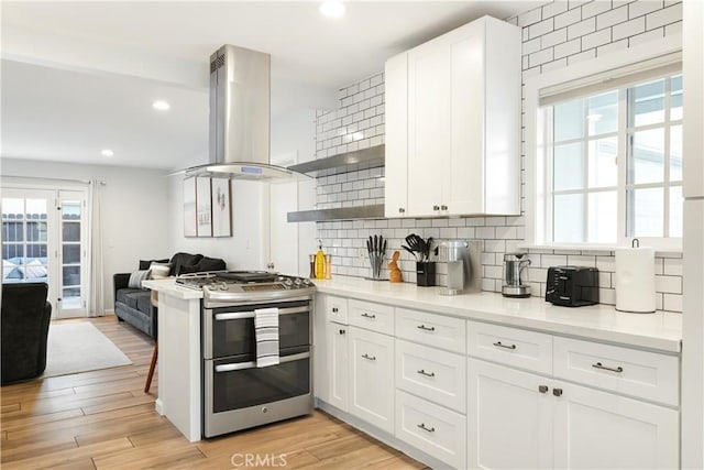 kitchen featuring island range hood, white cabinets, open floor plan, double oven range, and tasteful backsplash