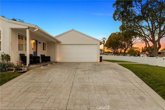 view of property exterior featuring decorative driveway, a yard, stucco siding, an attached garage, and fence