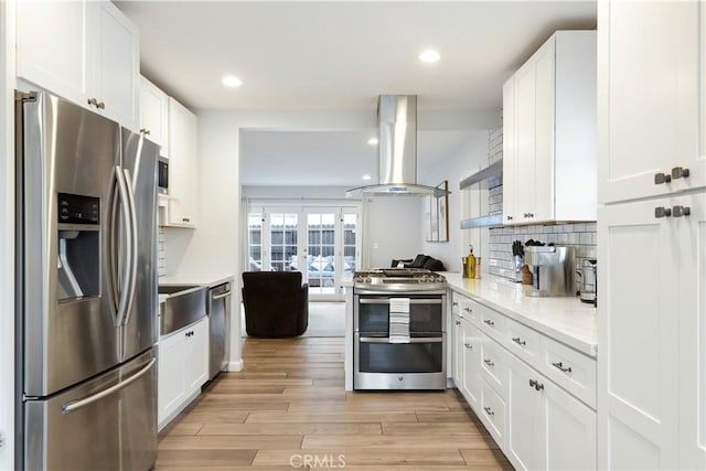 kitchen with stainless steel appliances, white cabinets, backsplash, and island range hood