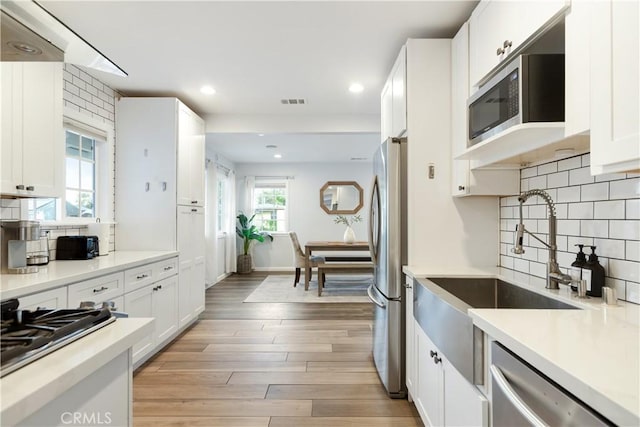 kitchen with stainless steel appliances, light countertops, white cabinets, and light wood-style flooring