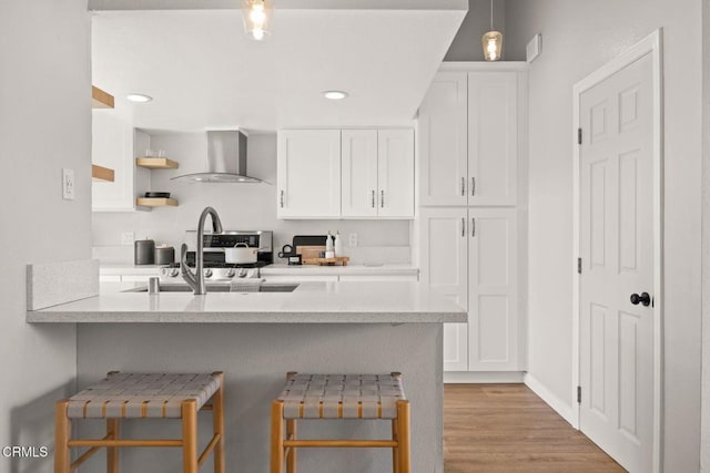 kitchen featuring wall chimney exhaust hood, a kitchen bar, and white cabinets