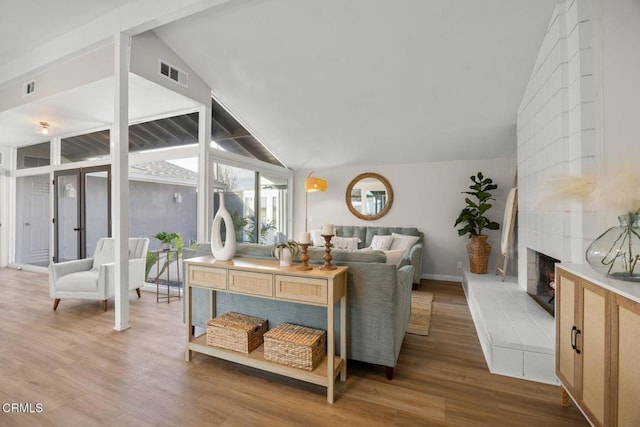 living room featuring lofted ceiling, wood finished floors, a tile fireplace, and visible vents