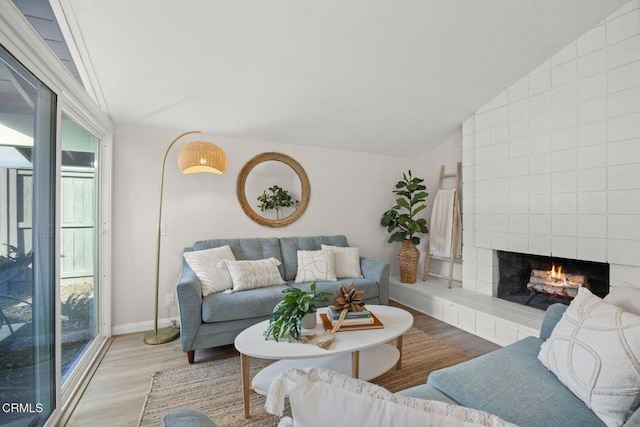 living area with a healthy amount of sunlight, a fireplace, vaulted ceiling, and wood finished floors