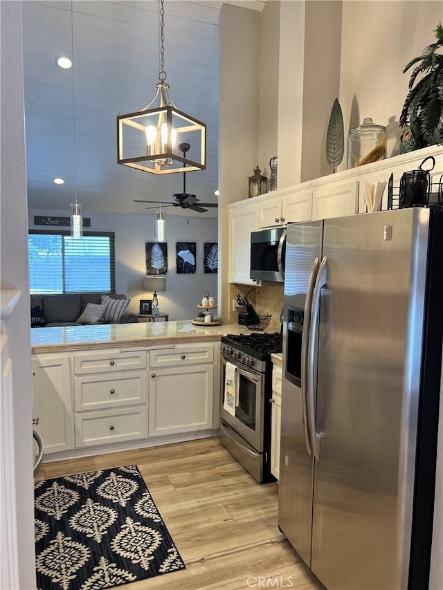 kitchen with white cabinets, appliances with stainless steel finishes, decorative light fixtures, light countertops, and light wood-style floors