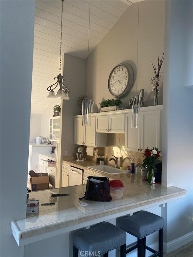 kitchen featuring a peninsula, a sink, white cabinetry, light countertops, and pendant lighting