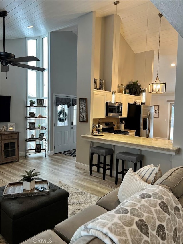 living area featuring high vaulted ceiling, wooden ceiling, light wood-style floors, and baseboards