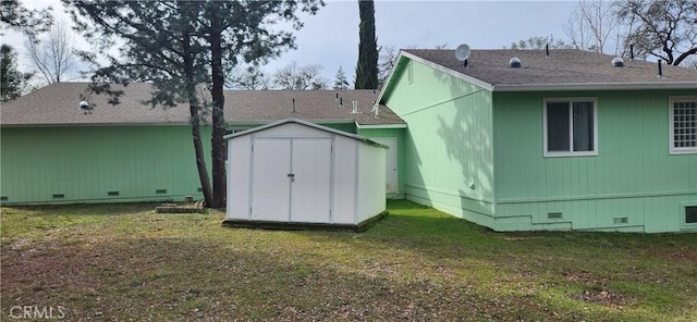 rear view of property with an outbuilding, a shingled roof, crawl space, a lawn, and a shed