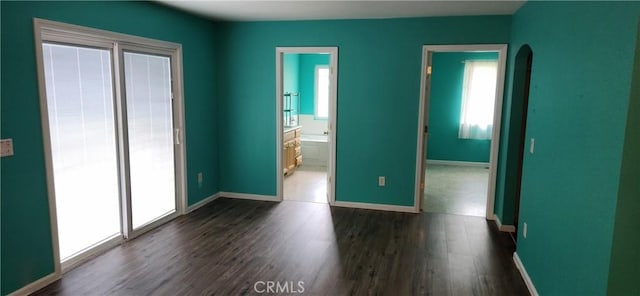 unfurnished bedroom with dark wood-type flooring, arched walkways, and baseboards