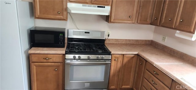 kitchen with light countertops, freestanding refrigerator, black microwave, under cabinet range hood, and stainless steel gas range oven