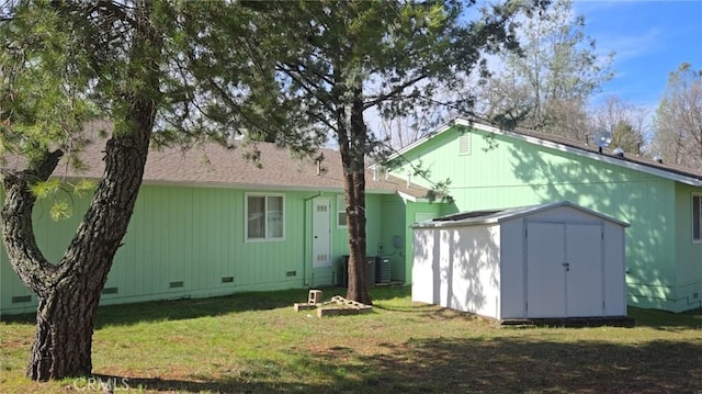 rear view of house featuring crawl space, a shed, a lawn, and an outbuilding