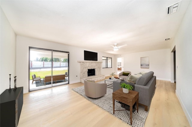 living area with light wood-style floors, baseboards, visible vents, and a stone fireplace