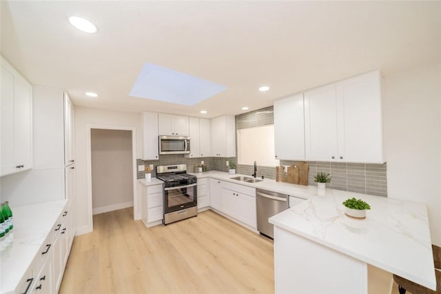 kitchen with a skylight, white cabinets, a peninsula, stainless steel appliances, and a sink