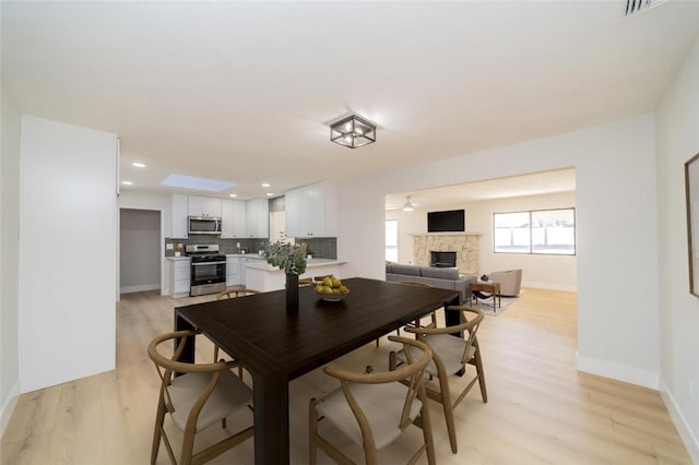 dining area featuring recessed lighting, light wood-style floors, a ceiling fan, a stone fireplace, and baseboards